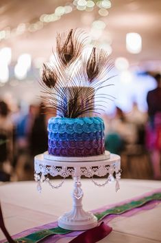 a multi - colored cake with peacock feathers on top sits on a table in a banquet hall