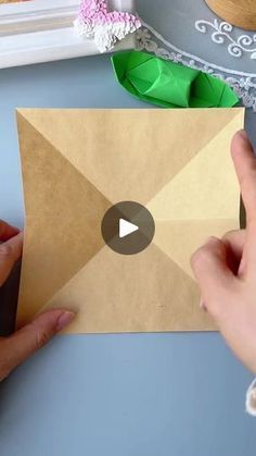 someone is making an origami envelope out of brown paper and some green leaves