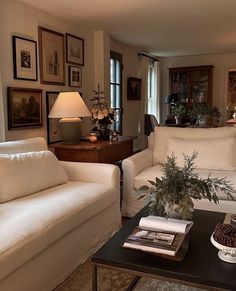 a living room filled with white furniture and pictures on the wall above it's coffee table