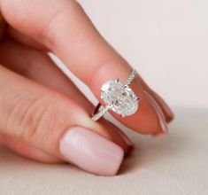 a woman's hand holding an engagement ring with a diamond on it and the band around her finger