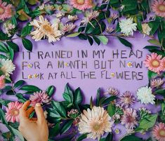 someone is writing on a purple wall with flowers and leaves around it that says it rained in my head for a month but now i look at all the flowers