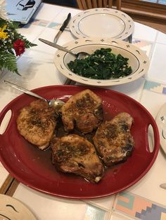 a red plate topped with meat next to a bowl of spinach and other dishes