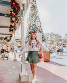 a woman standing in front of a christmas tree wearing a santa clause sweater and skirt