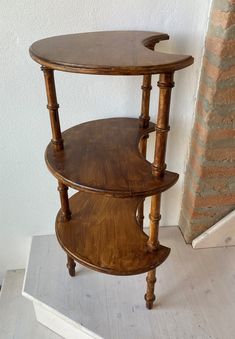 two tiered wooden table sitting on top of a white floor next to a brick wall