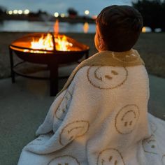 a little boy wrapped in a towel sitting next to a fire pit