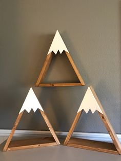 three wooden triangle shaped shelves with white mountains on each side and one in the middle