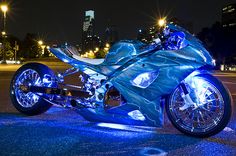 a shiny blue motorcycle is parked on the side of the road at night with city lights in the background