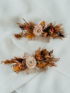 two hair combs with dried flowers and leaves on top of a white cloth background