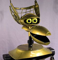 a golden robot sitting on top of a black chair with eyes painted on it's head