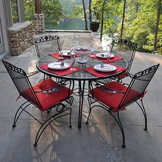 an outdoor table with red chairs and plates on it