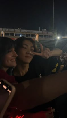 two people taking pictures with their cell phones at a baseball game in the night time