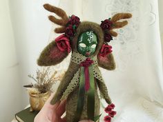 a hand holding a small doll with flowers on it's head and antlers in her hair