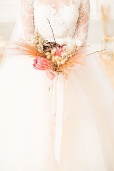 a woman in a white wedding dress holding a bouquet with feathers and flowers on it