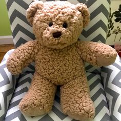 a brown teddy bear sitting on top of a blue and white chair with chevron fabric