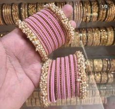 pink and gold bracelets are being held by someone's hand in front of several rows of bangles