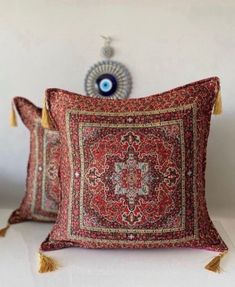 two decorative pillows with tassels on top of each one and an evil eye in the middle