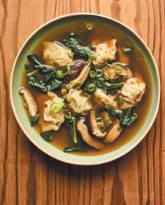 a green bowl filled with dumplings and vegetables on top of a wooden table next to a spoon