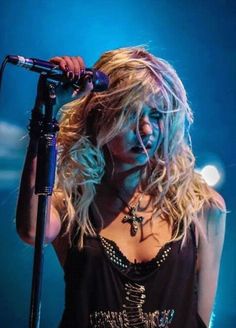 a woman with blonde hair holding a microphone in her hand and singing into the microphone