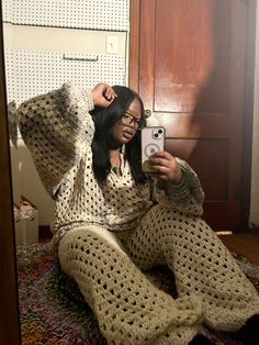 a woman is sitting on the floor taking a selfie with her cell phone while wearing knitted pajamas