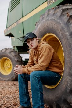 a young man sitting on the rim of a large green tractor with his hands in his pockets