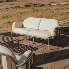 two chairs and a couch sitting on a wooden deck in the middle of an open field