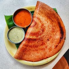 a white plate topped with two pieces of food next to dipping sauces and green leaves