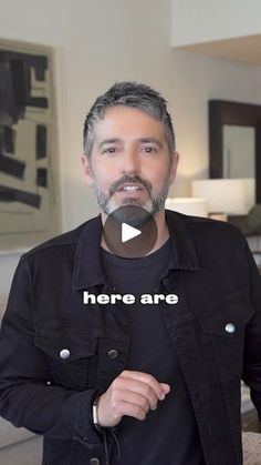 a man standing in front of a couch with the words here are on his shirt