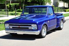 an old blue truck parked on the side of the road in front of a house