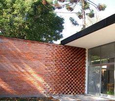 a brick wall in front of a building with glass doors and large trees behind it