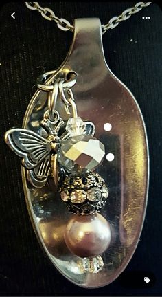 a glass bottle with some pearls and a butterfly on it's side, hanging from a chain