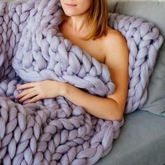 a woman wrapped up in a giant chunky blanket on a couch with her arms folded out