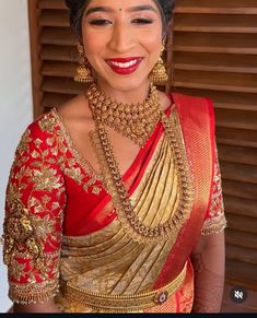 a woman in a red and gold sari with jewelry on her neck, smiling at the camera