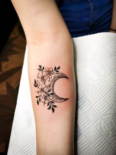 a woman's arm with a tattoo on it that has a crescent moon and flowers