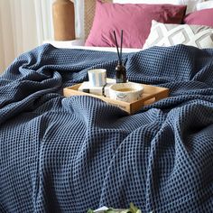 a tray with two cups on top of it sitting on a bed covered in blue blankets