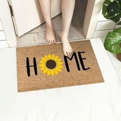 a door mat with the words home and a sunflower on it next to a woman's feet