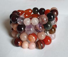 This is indeed an attractive eye candy. The crystals used in the making of this bracelet display the colors of fall - bright orange, russet red, pink and yellow. This unique memory bracelet comprises a medley of 10 mm carnelian, multi coloured tiger's eye, phantom amethyst and rose quartz crystals as well as 8 mm sunstone and garnet beads. It is accented with silver accents, Swarovski crystals and flower charms which gives it a fashionable outlook. A nice chunky piece of bracelet to have to brighten your plain attire or complement your gaudy ones,  This medley of crystals bracelet provides a burst of colour and complements any attire.   Fits a size 15 to 16 cm wrist. Handmade Wrap Bracelet With Round Beads For Healing, Handmade Orange Agate Bracelets, Handmade Orange Agate Bracelet, Spiritual Hand Wrapped Orange Jewelry, Handmade Carnelian Round Bead Bracelets, Handmade Orange Agate Beaded Bracelets, Handmade Spiritual Orange Stretch Bracelet, Handmade Carnelian Bracelets, Handmade Agate Crystal Bracelet Spiritual