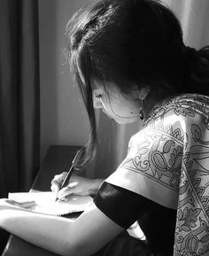 a woman writing on a piece of paper with a pen in her hand while sitting at a desk