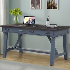 a laptop computer sitting on top of a wooden desk next to a vase with flowers