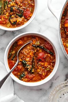 two bowls of vegetable soup on a marble table with silver spoons and napkins