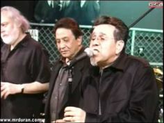 three men standing next to each other with microphones in their hands and one man singing