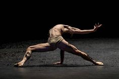 a male dancer is performing in the dark with his arms stretched out and legs spread wide