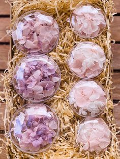 four glass bowls filled with pink and white flowers on top of a wooden table next to straw