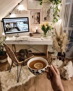 a person holding a cup of coffee in front of a desk with pictures on the wall