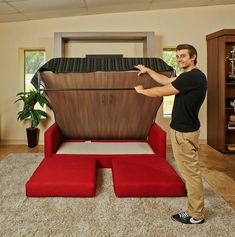 a man standing next to a red couch in a living room with an ottoman on it