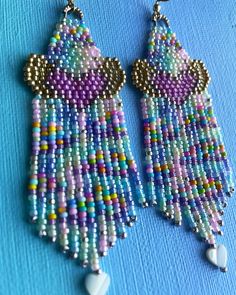 the beaded earrings are hanging from hooks on a blue surface with white beads and silver earwires