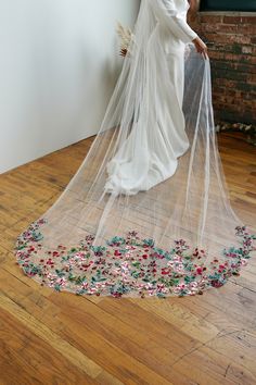 a woman in a wedding dress with a veil over her head and flowers on the floor