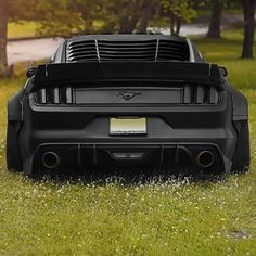 the rear end of a black sports car parked on grass with trees in the background