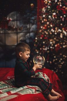 a young boy sitting on top of a bed holding a crystal ball in front of a christmas tree