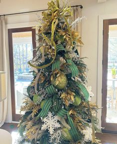 a decorated christmas tree with gold and green ornaments on it's top, in front of a window