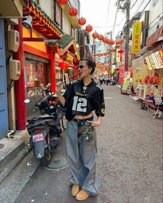 a woman standing on the side of a street next to parked motorcycles and shops with red lanterns in the background